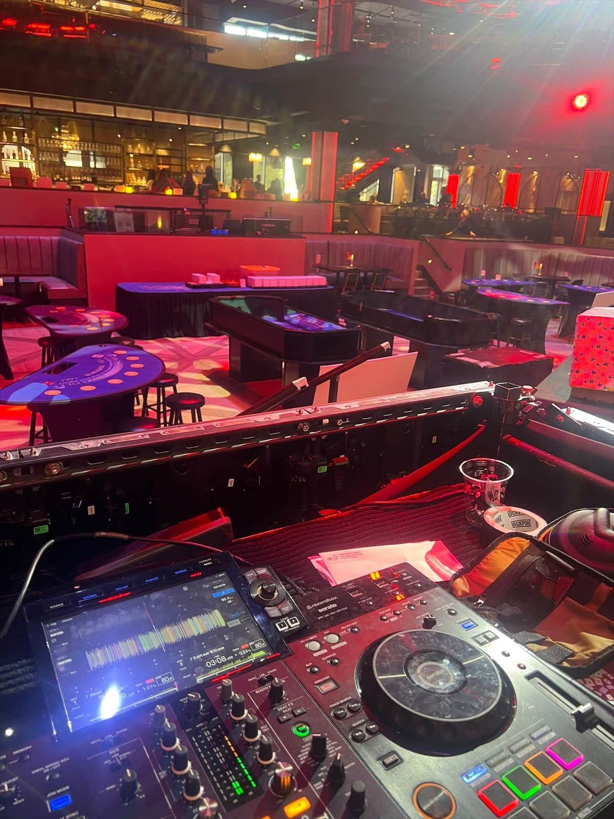 DJ controller on a booth overlooking a red-lit club floor with game tables