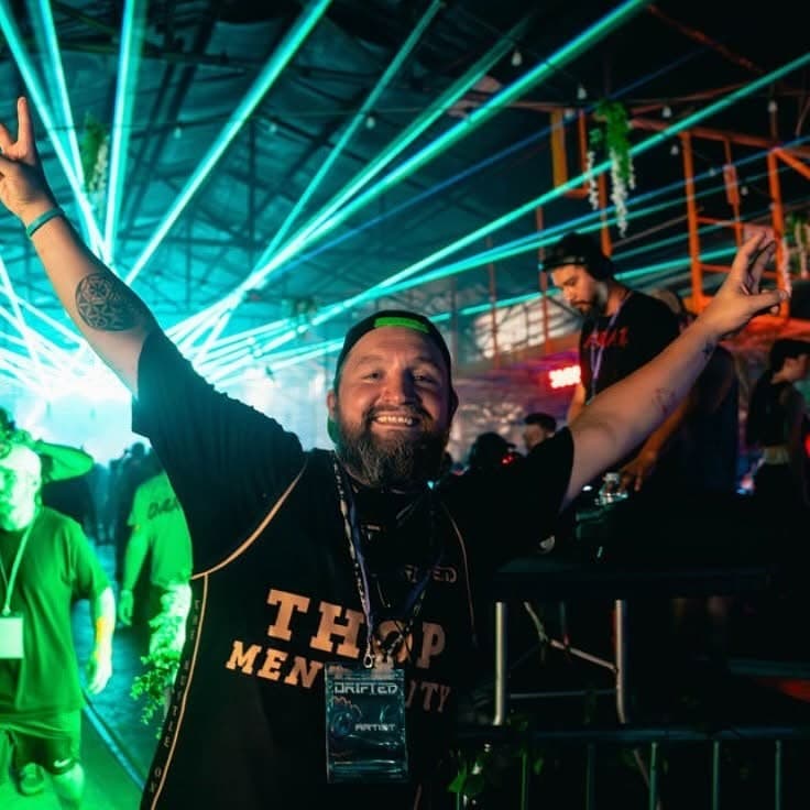 DJ with both arms raised under green laser beams at a festival