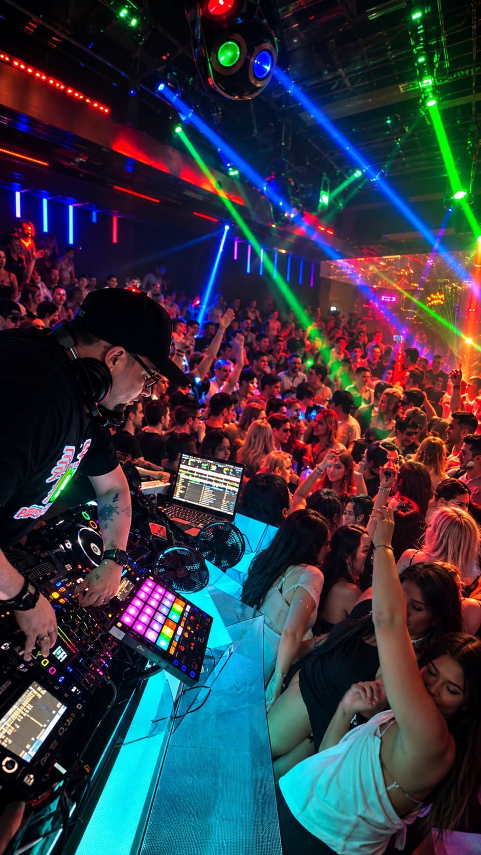 DJ at the decks with green and blue lasers over a packed dance floor
